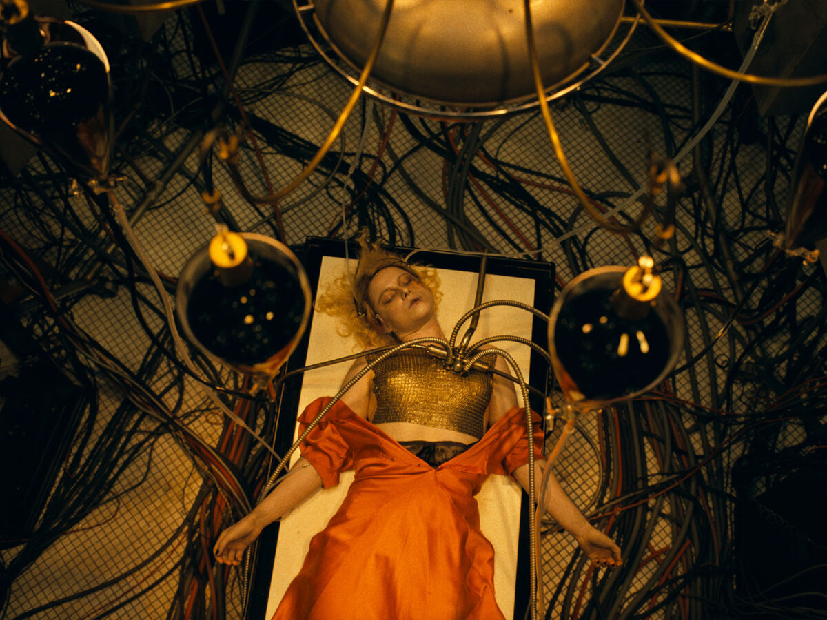 Jessie Buckley as "The Bride" in the film of the same name, laying on a surgical table with medical equipment attached to her body.